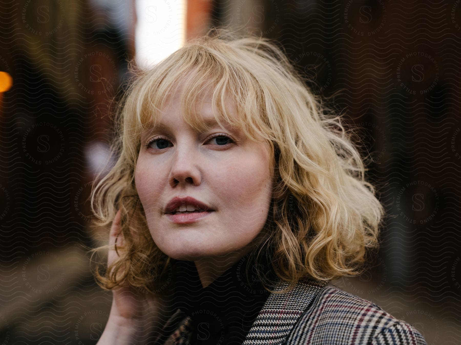 A Caucasian woman, with blonde hair and donned in a blazer suit, is positioned in the center of the road.  A blonde-haired Caucasian woman, dressed in a blazer suit, stands amidst the street.