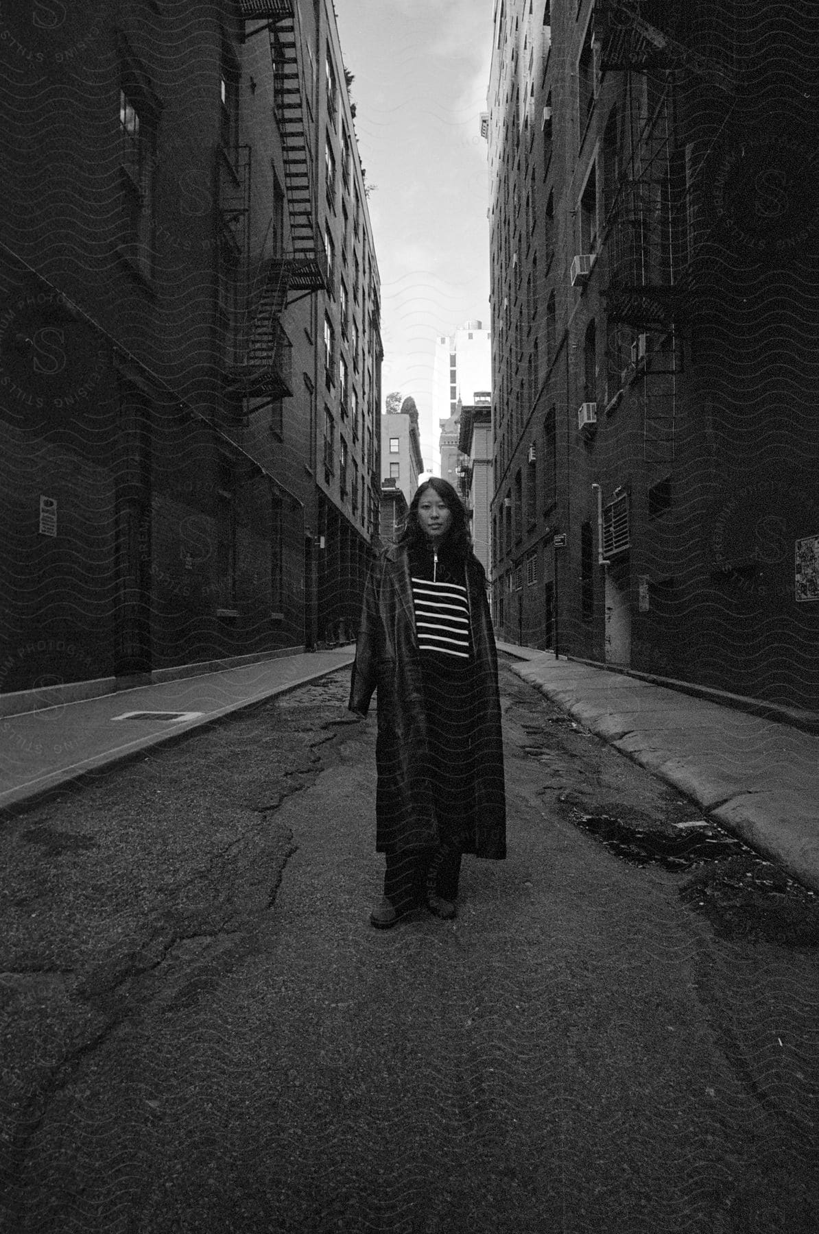 Woman wearing a long coat standing in alley between apartment buildings