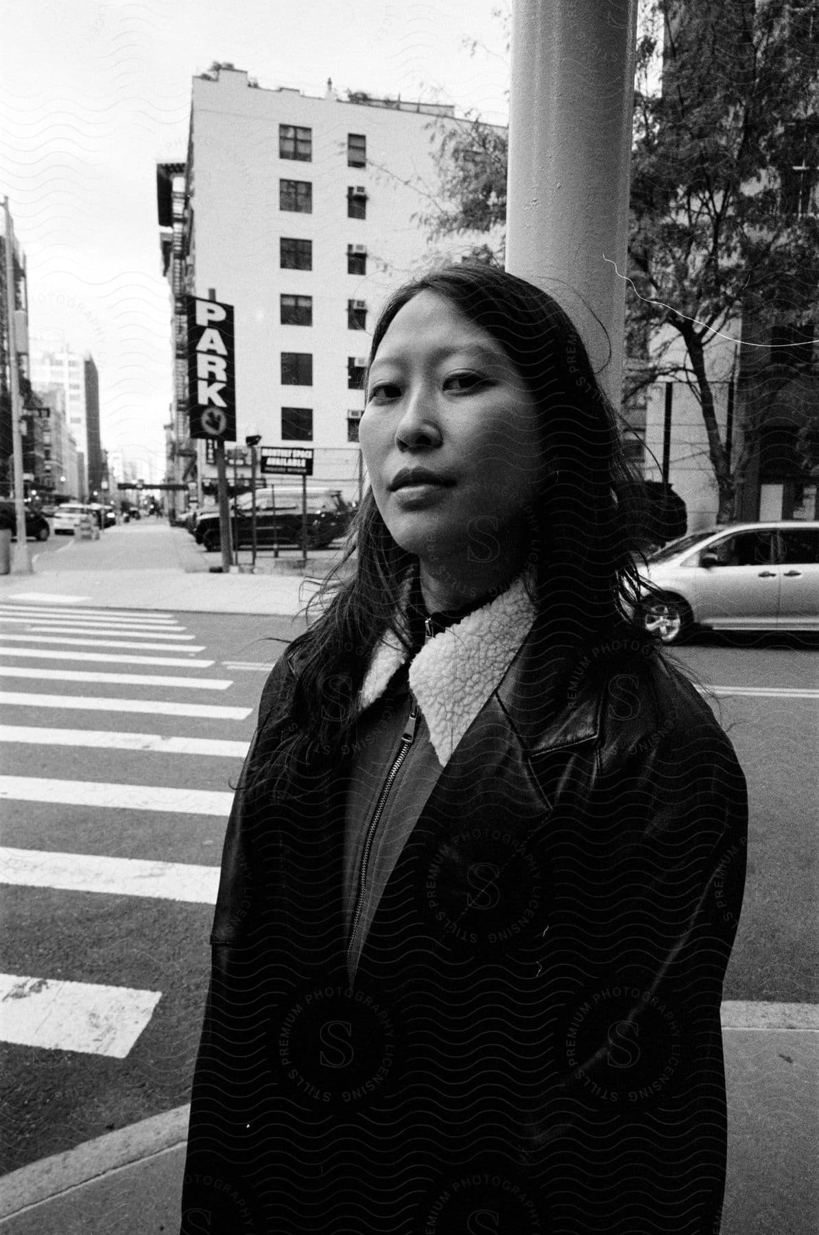 A woman in a leather jacket stands at a downtown city intersection