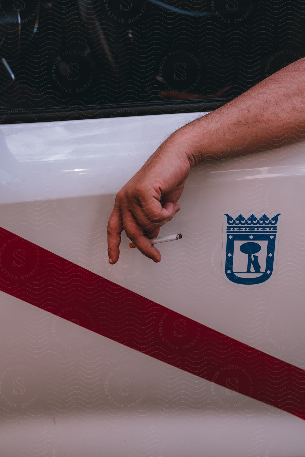 Person arm holding a cigarette next to the door of a taxi.