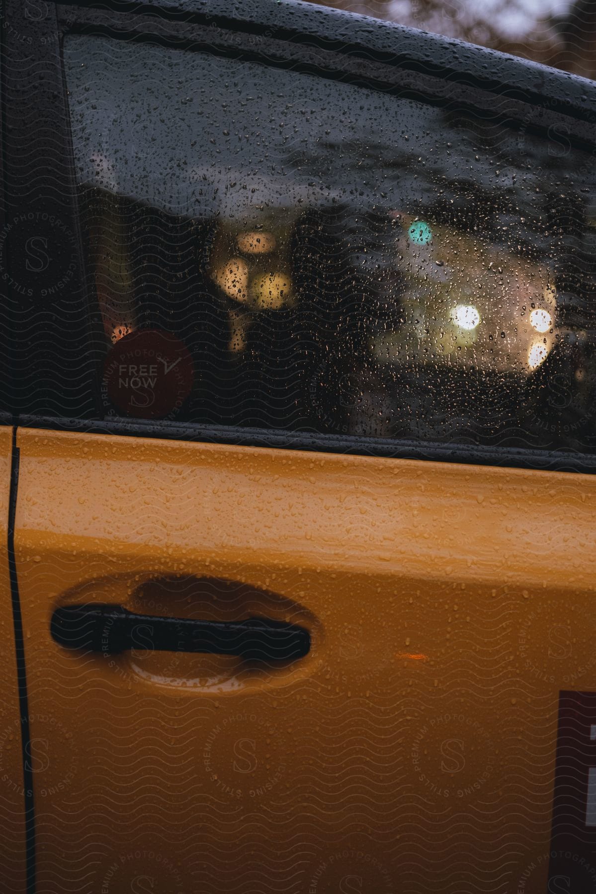 Side of the window of a yellow car with raindrops and a driver.