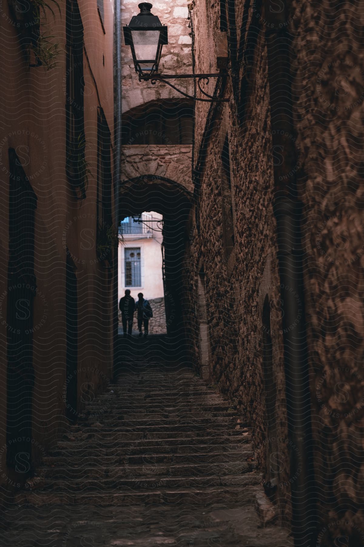 Two people going down steps in an alley between a smooth wall and a rough wall