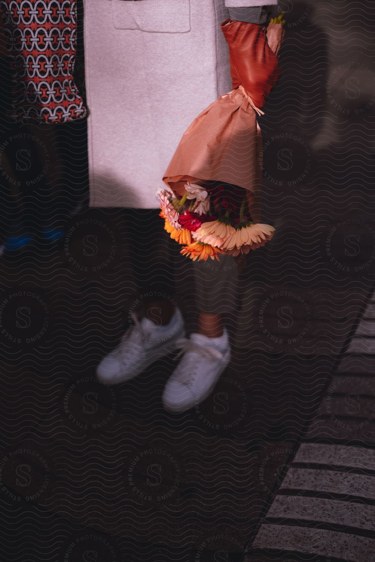 A person holding a bouquet of flowers wrapped in brown paper on a sidewalk