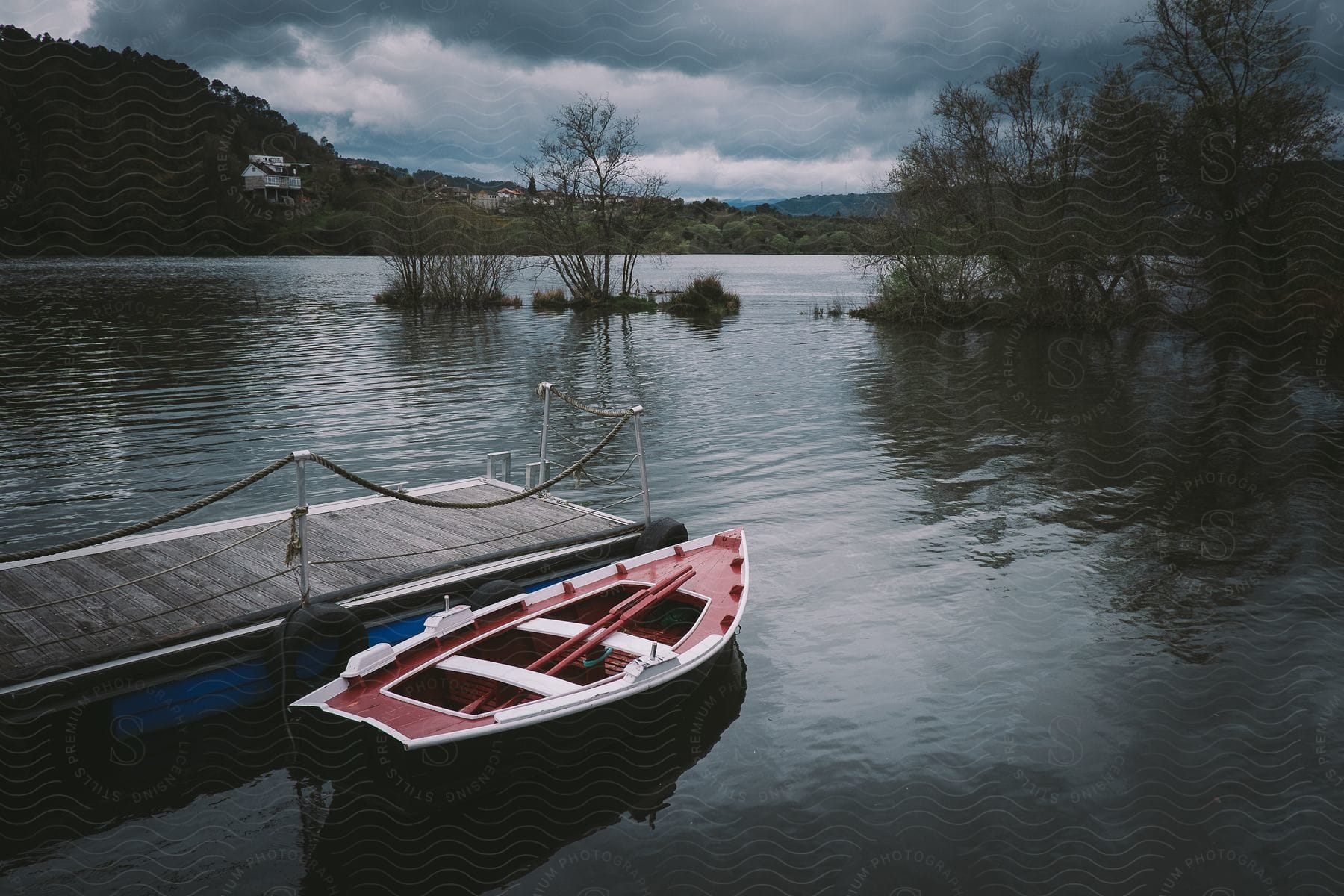 A red and white canoe is tied to a wooden dock on a lake on a dark, cloudy day.