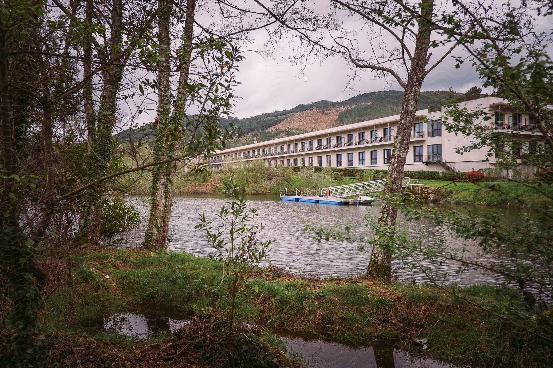 Calm river with vegetation on the banks and a blue and white boat and a building structure in the background.