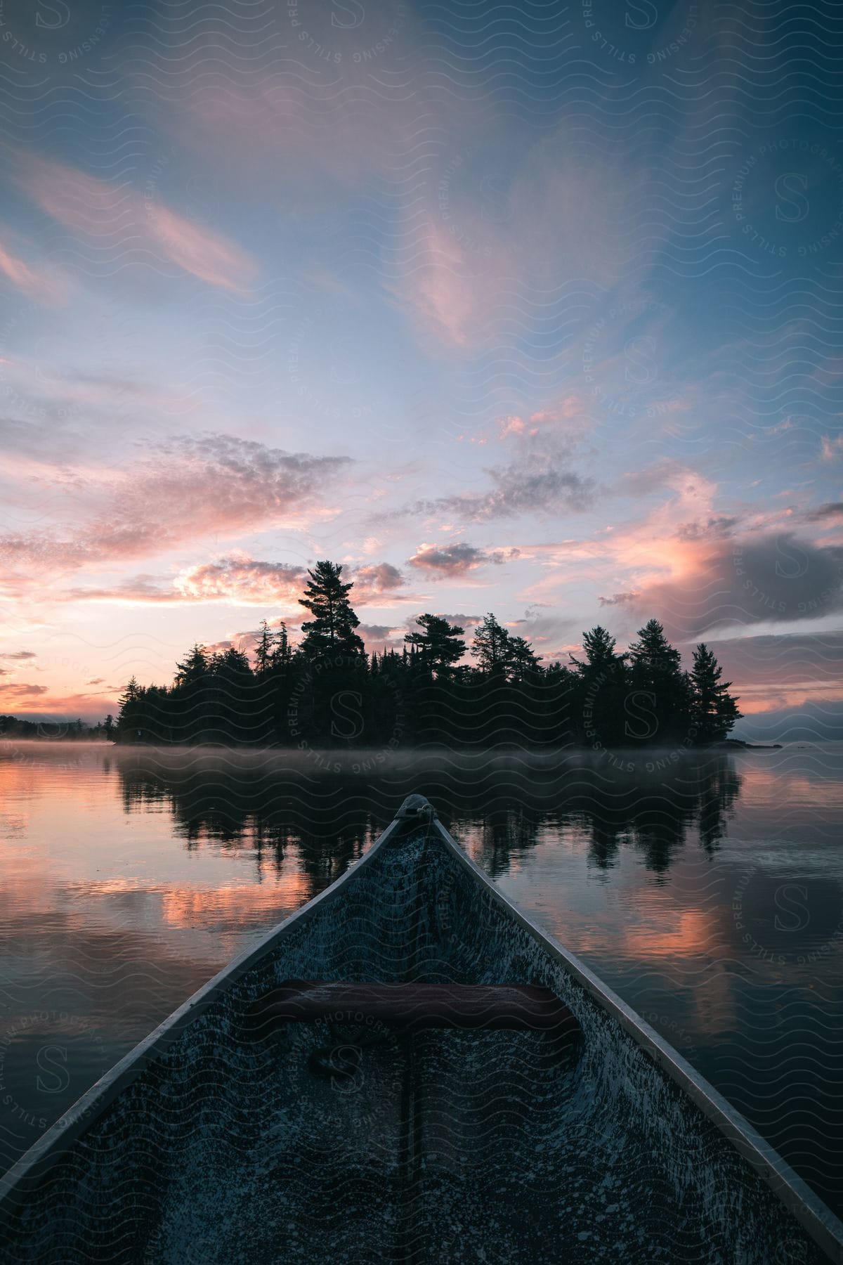 Bow of a canoe sailing towards a wooded island under a reddish dawn sky.