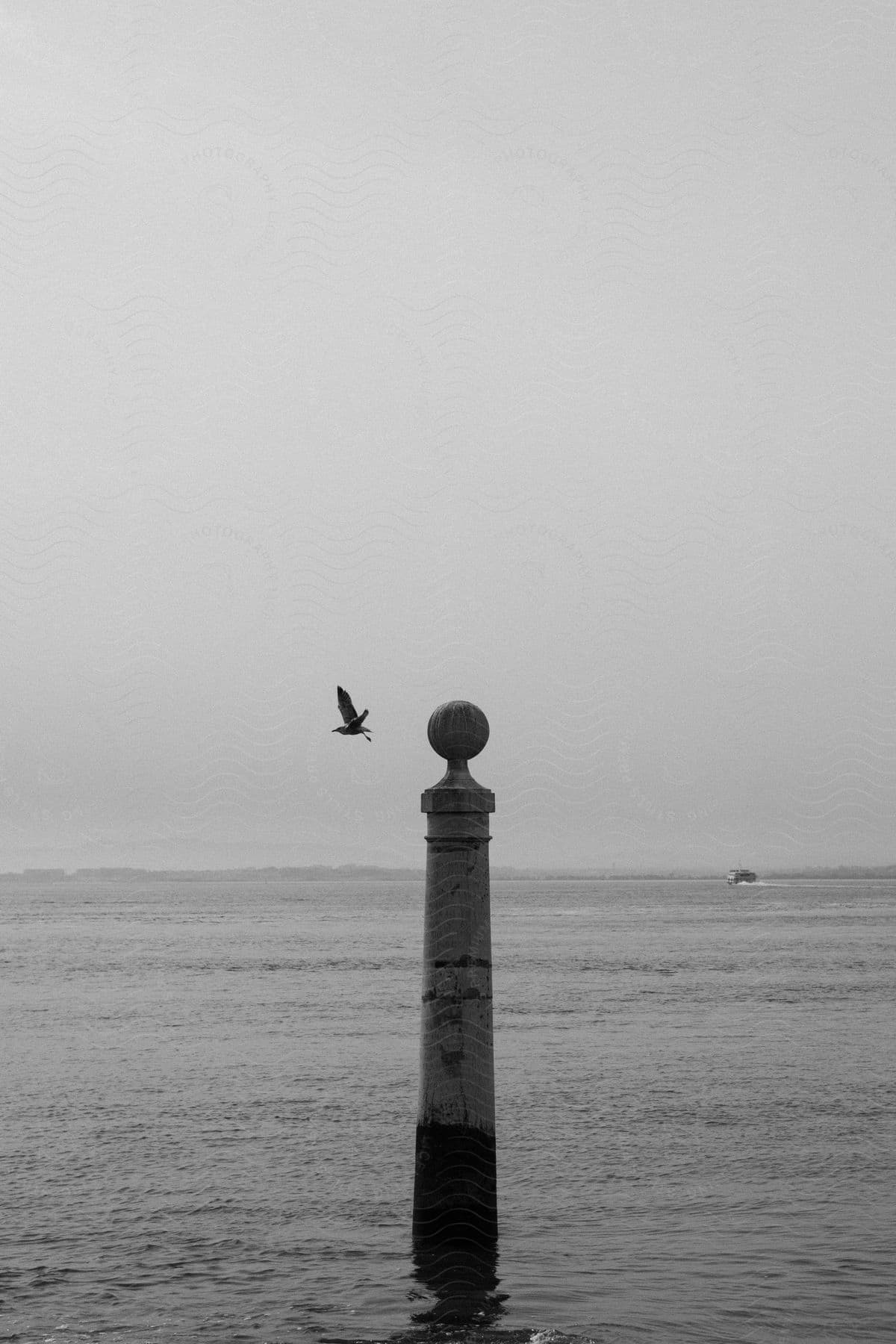 Lone post with a sphere on top in the middle of the ocean with a bird flying nearby.