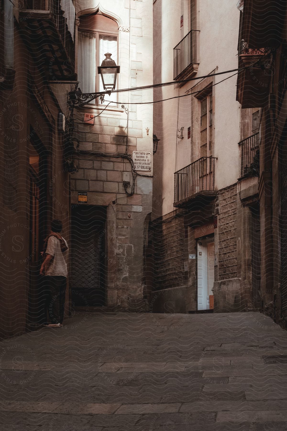 A young boy in a white shirt stands at the door of an establishment in an alley with several doors around it