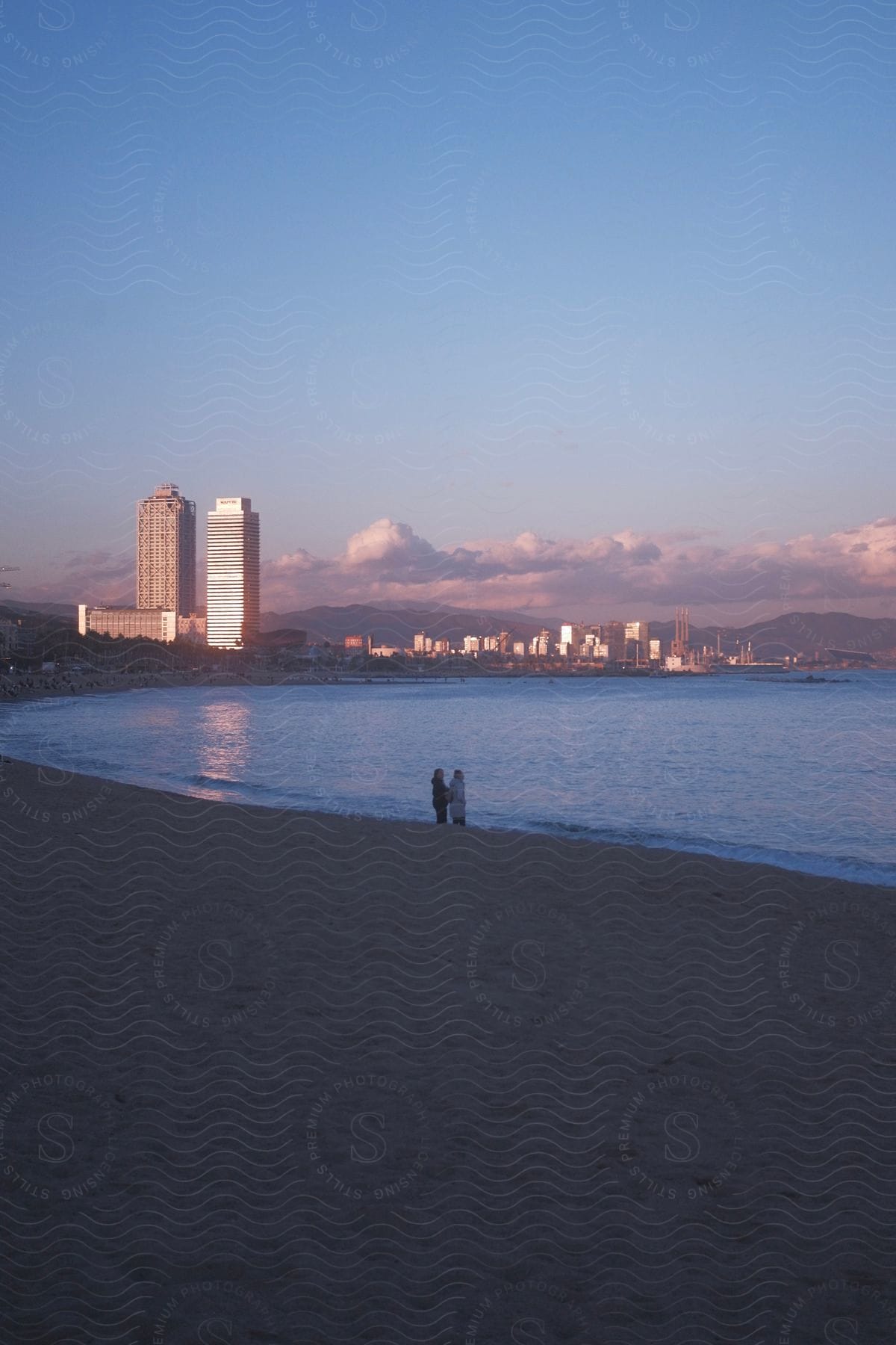 man and woman are silhouetted against the colorful blue sea as they stand on the beach with city skyline in the background