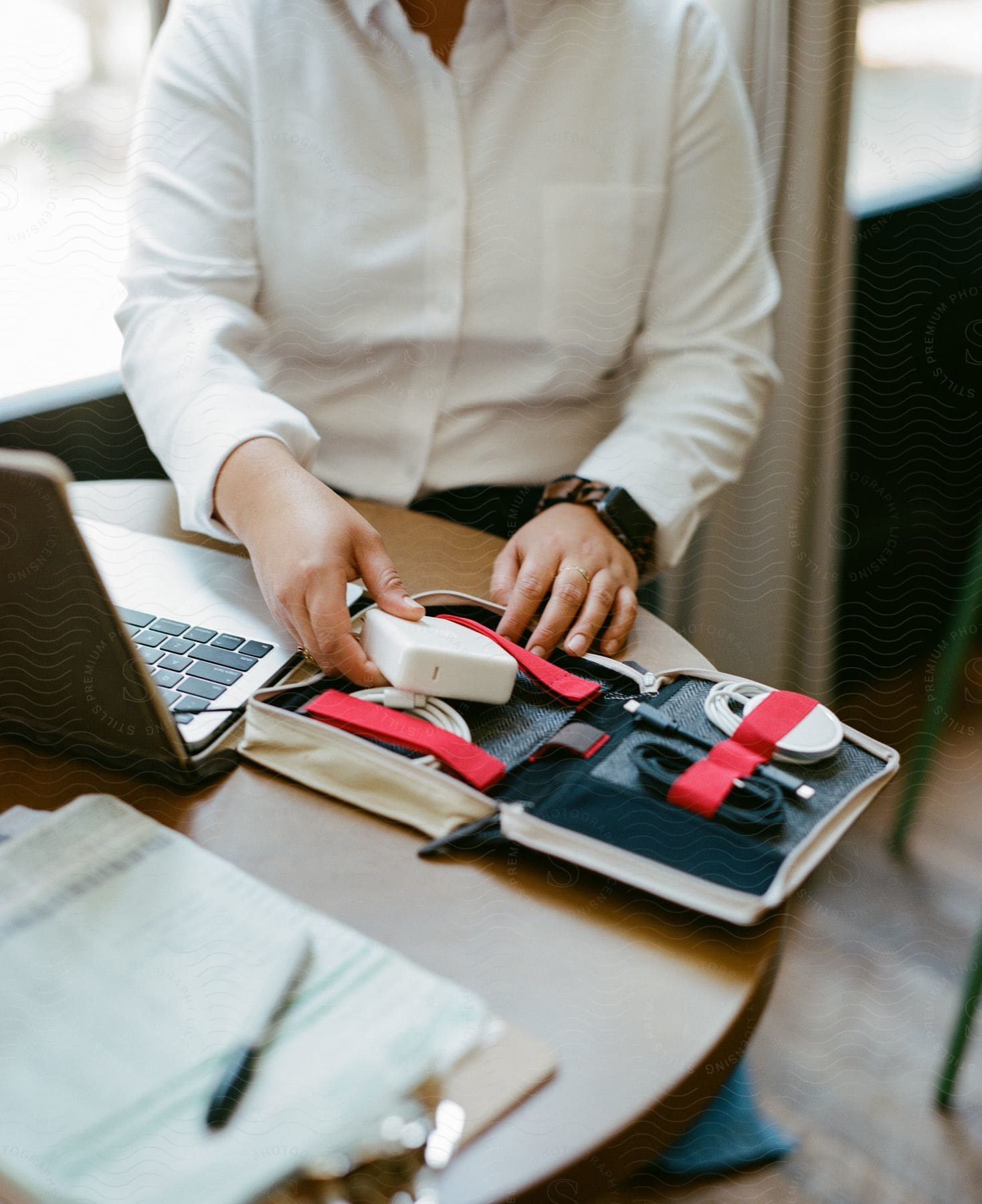 Woman sitting at a table with a laptop computer as she takes accessories from a small case