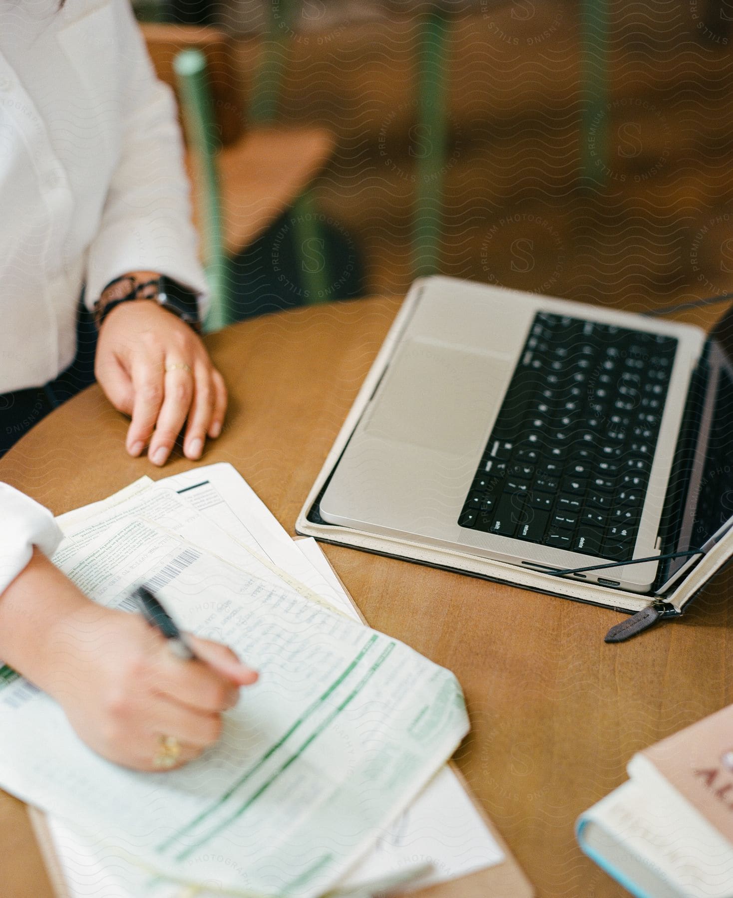 woman is writing on papers while standing at a table with a laptop