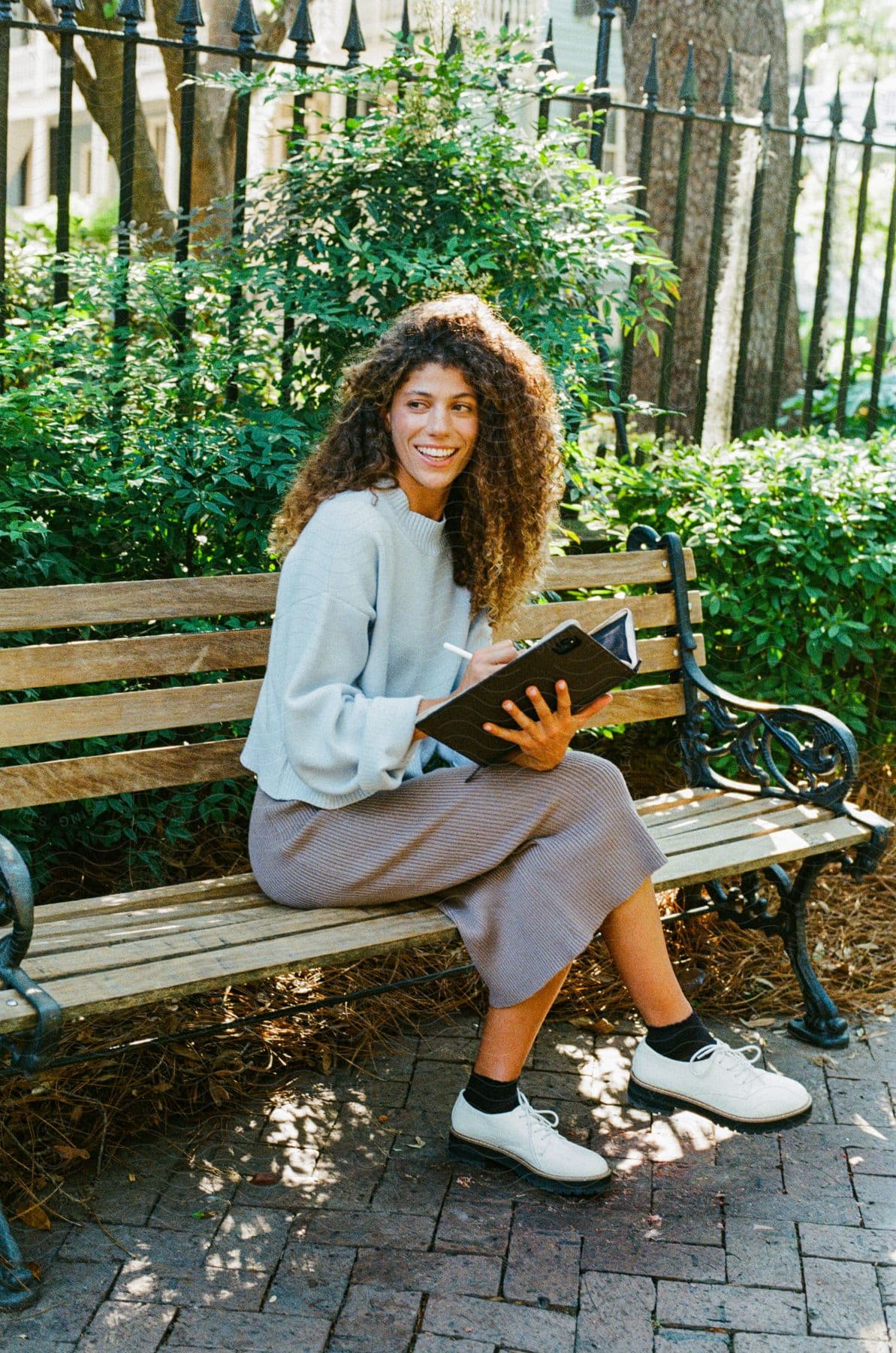 woman with curly hair poses on park bench holding notebook