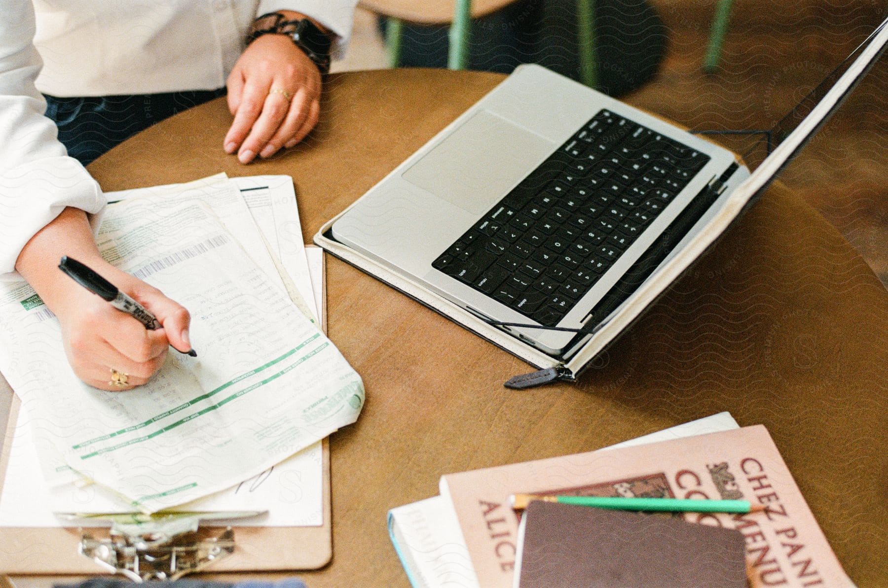 Wooden table with a woman's hands writing and a silver laptop next to it