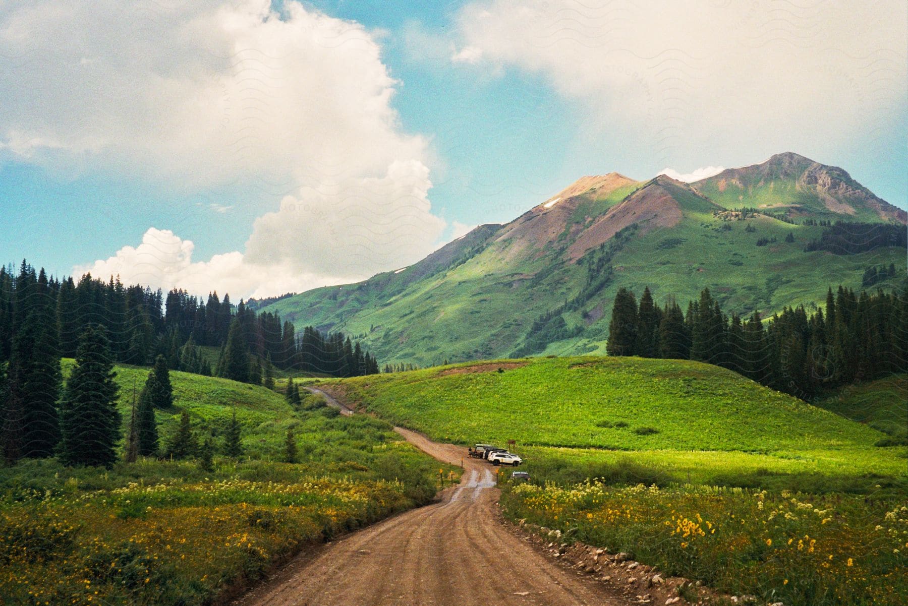 A dirt road across a grass field, leading to a mountain, with an ATV stopped to the road's side.