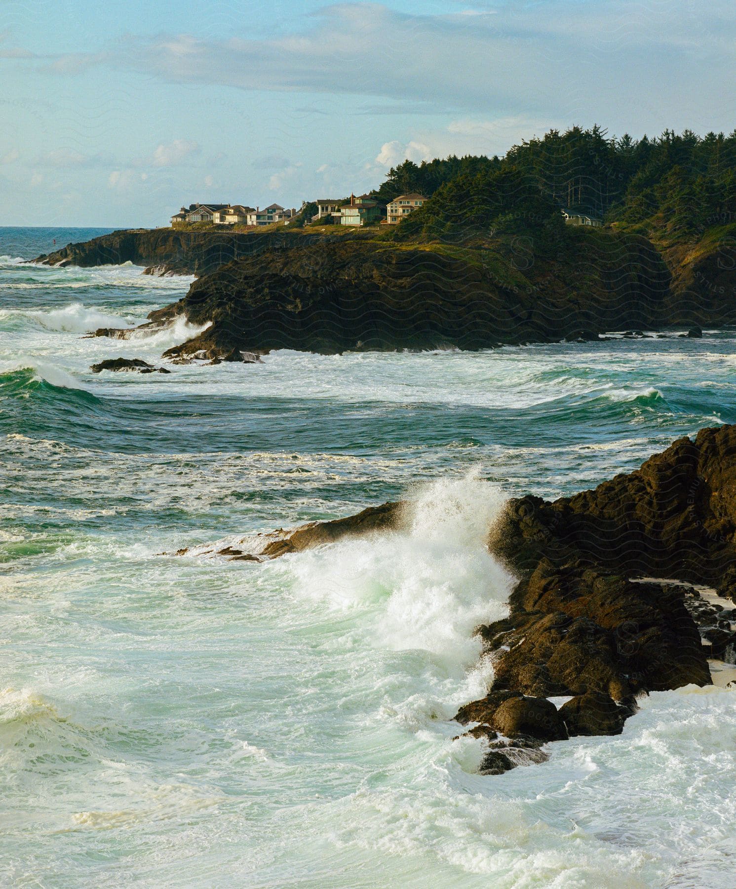 The powerful waves crash against the rocky shoreline with a coastal town, sending spray high into the air.