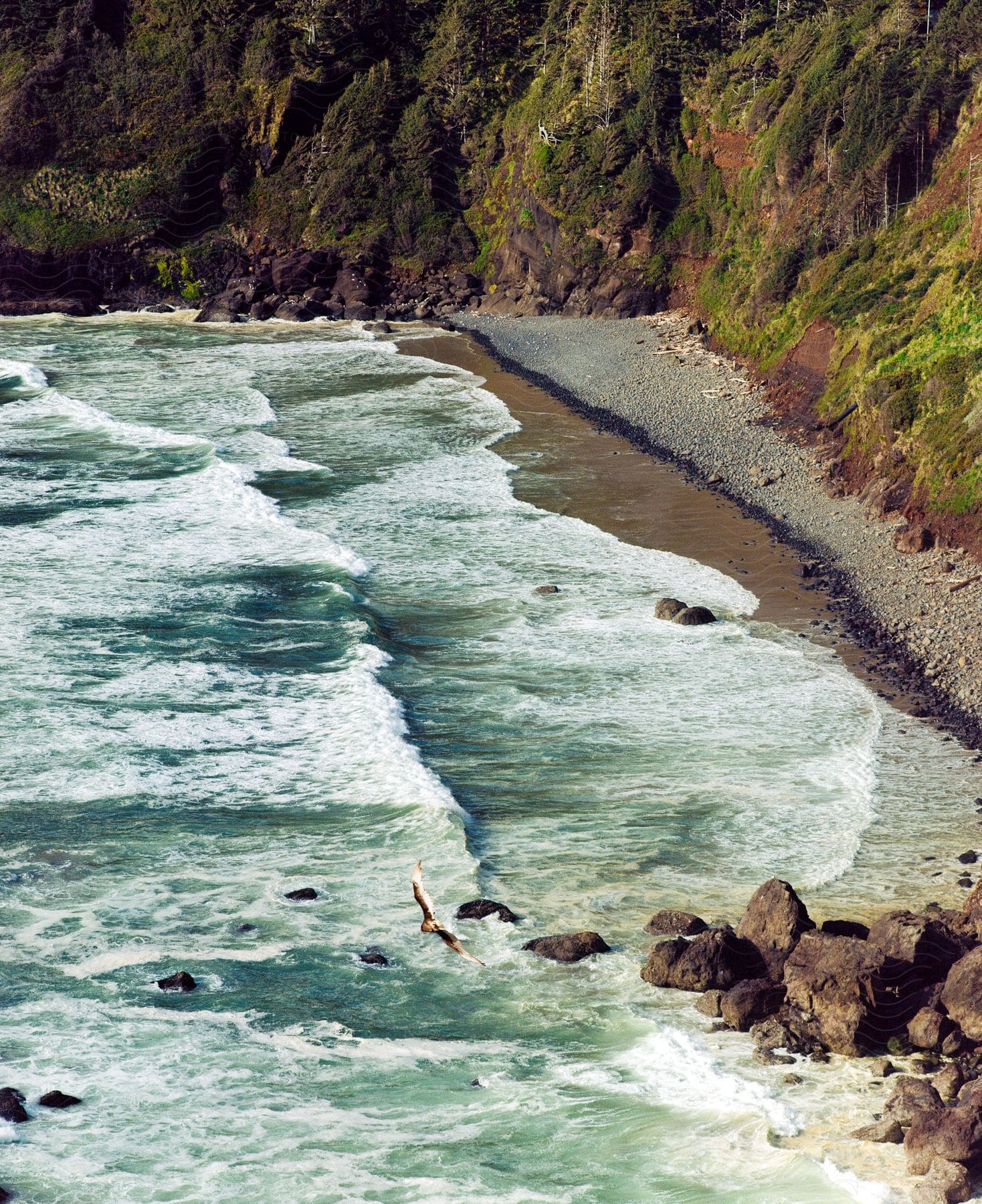 Waves crash against a highland beach, where grass-covered hills meet the shoreline.