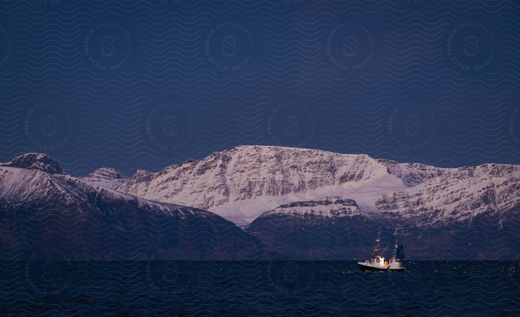 A boat sailing near a snowy mountain range.