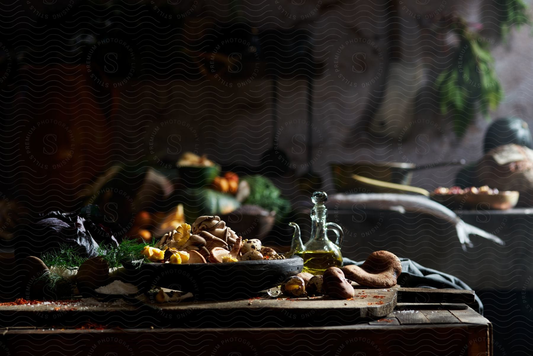 A rustic wooden table holds a bowl filled with earthy-colored mushrooms and a pool of golden olive oil, with fish near a saucepan and culinary utensils in the kitchen.