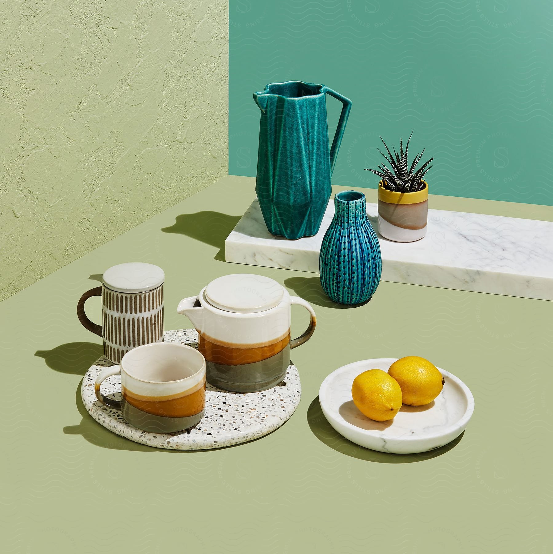 Teapots and mugs next to lemons on a beige countertop .