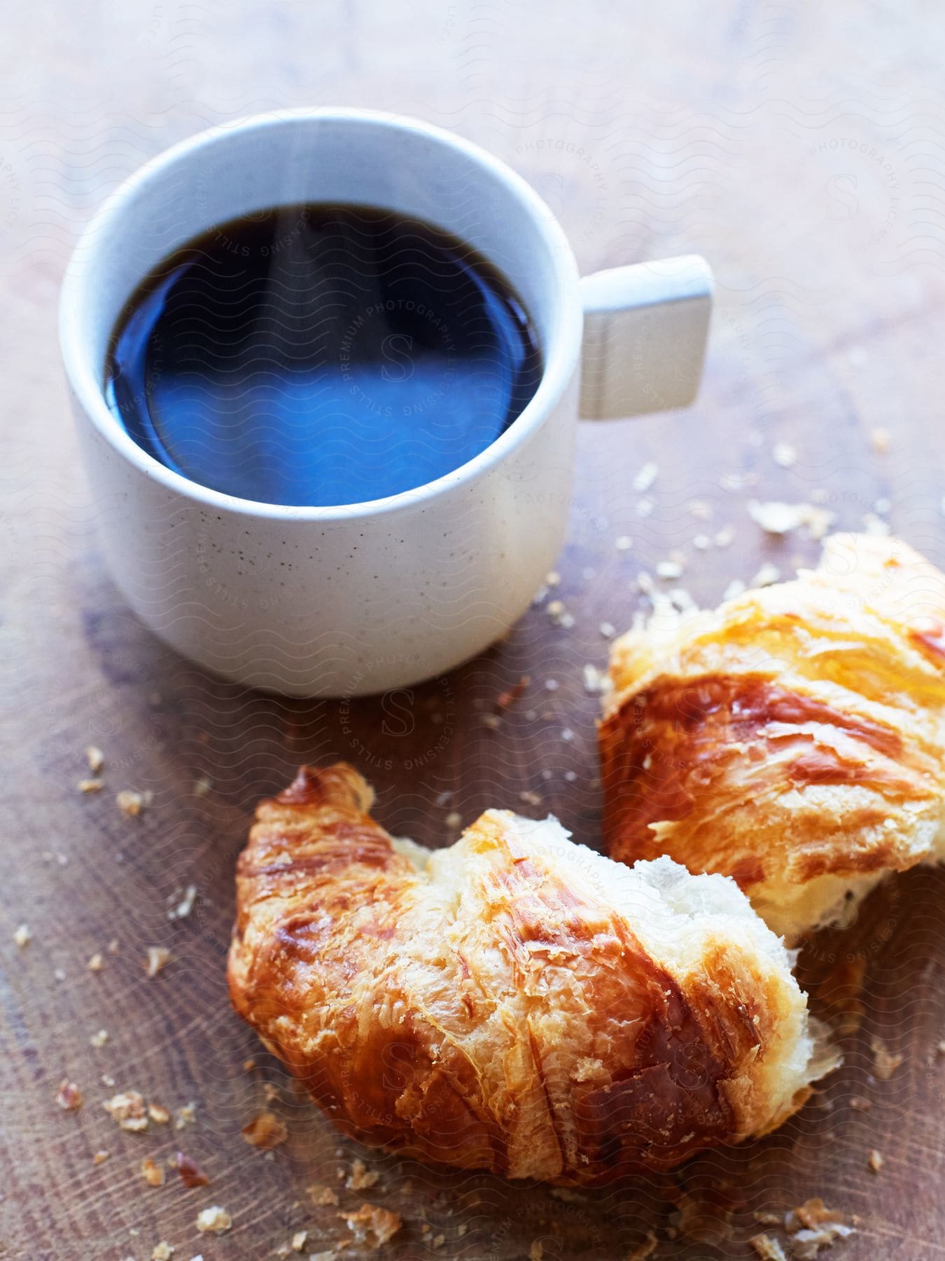 A simple breakfast of two croissants and a cup of coffee sits on a wooden table.