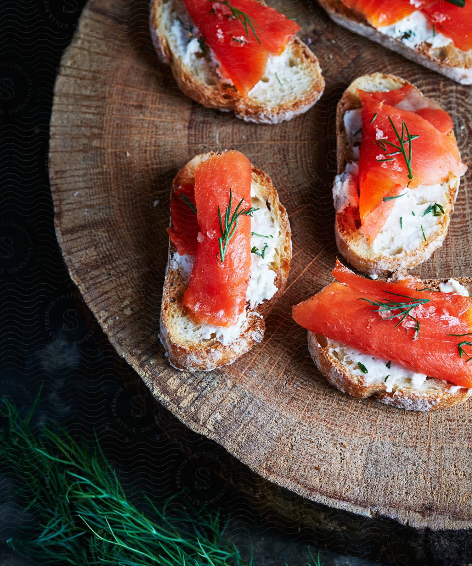 Five pieces of crusty bread sit on a cut tree trunk and each is covered with cream and a slice of something orange.