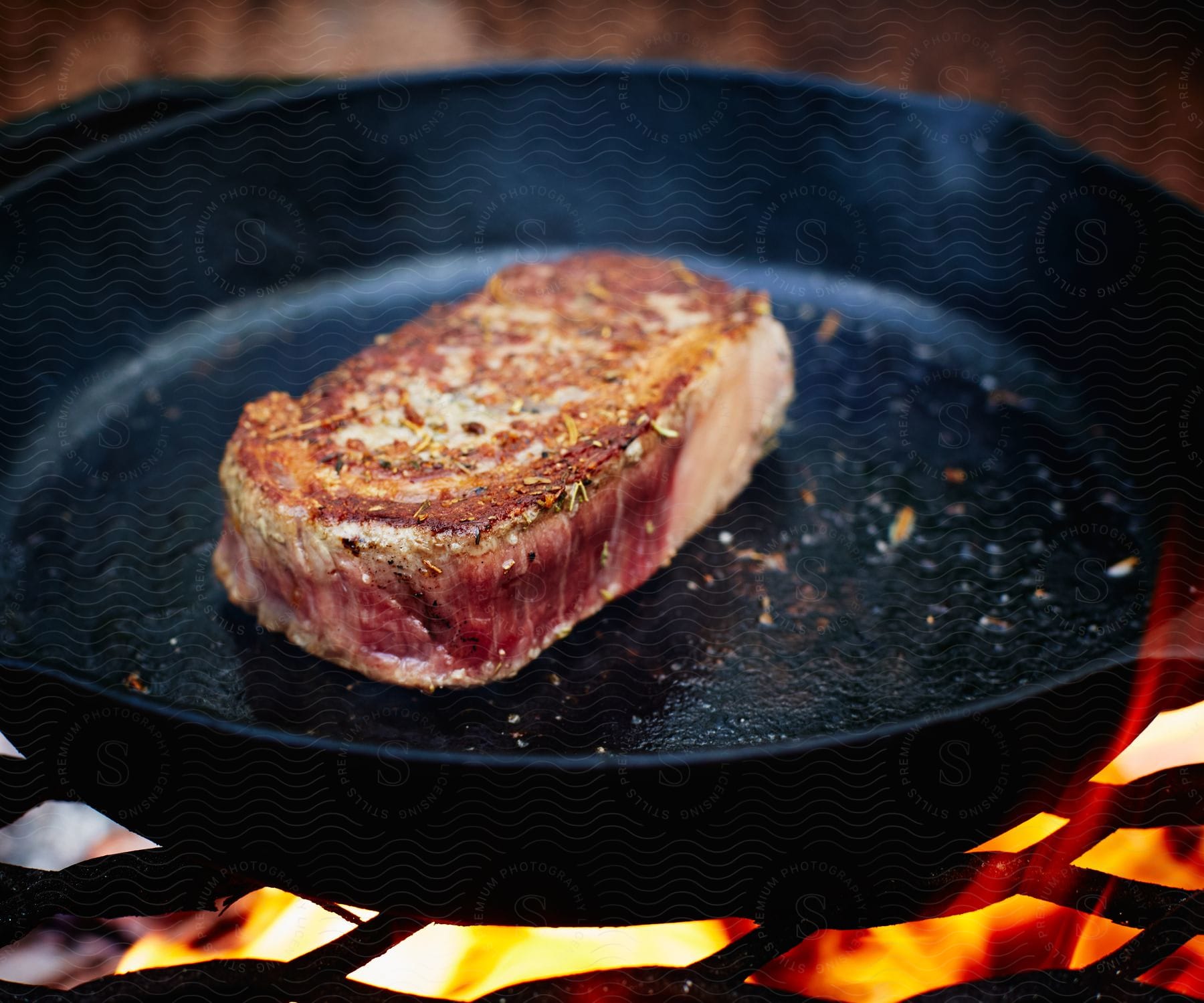 A juicy steak sizzles in a cast iron skillet over a bed of hot coals.