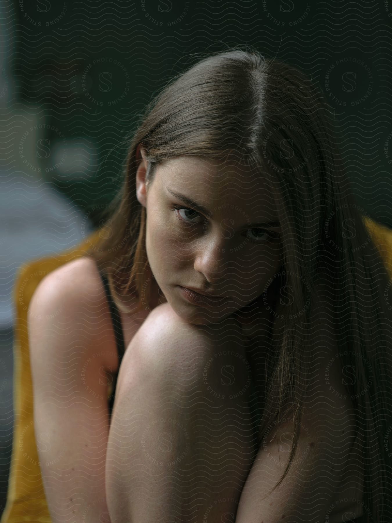 A girl with brown straight hair puts her knee on a yellow armchair as she sits