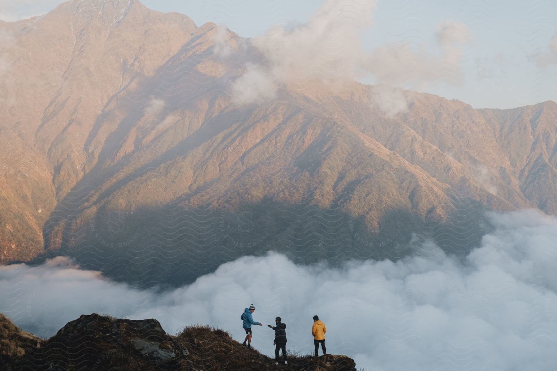 Three people standing on a ledge across from mountains high in the clouds