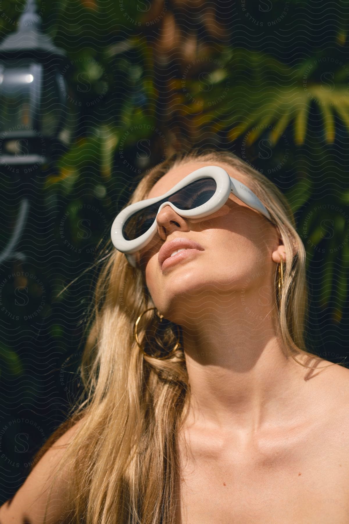 Stock photo of the person wearing white glasses is outdoors, surrounded by greenery.