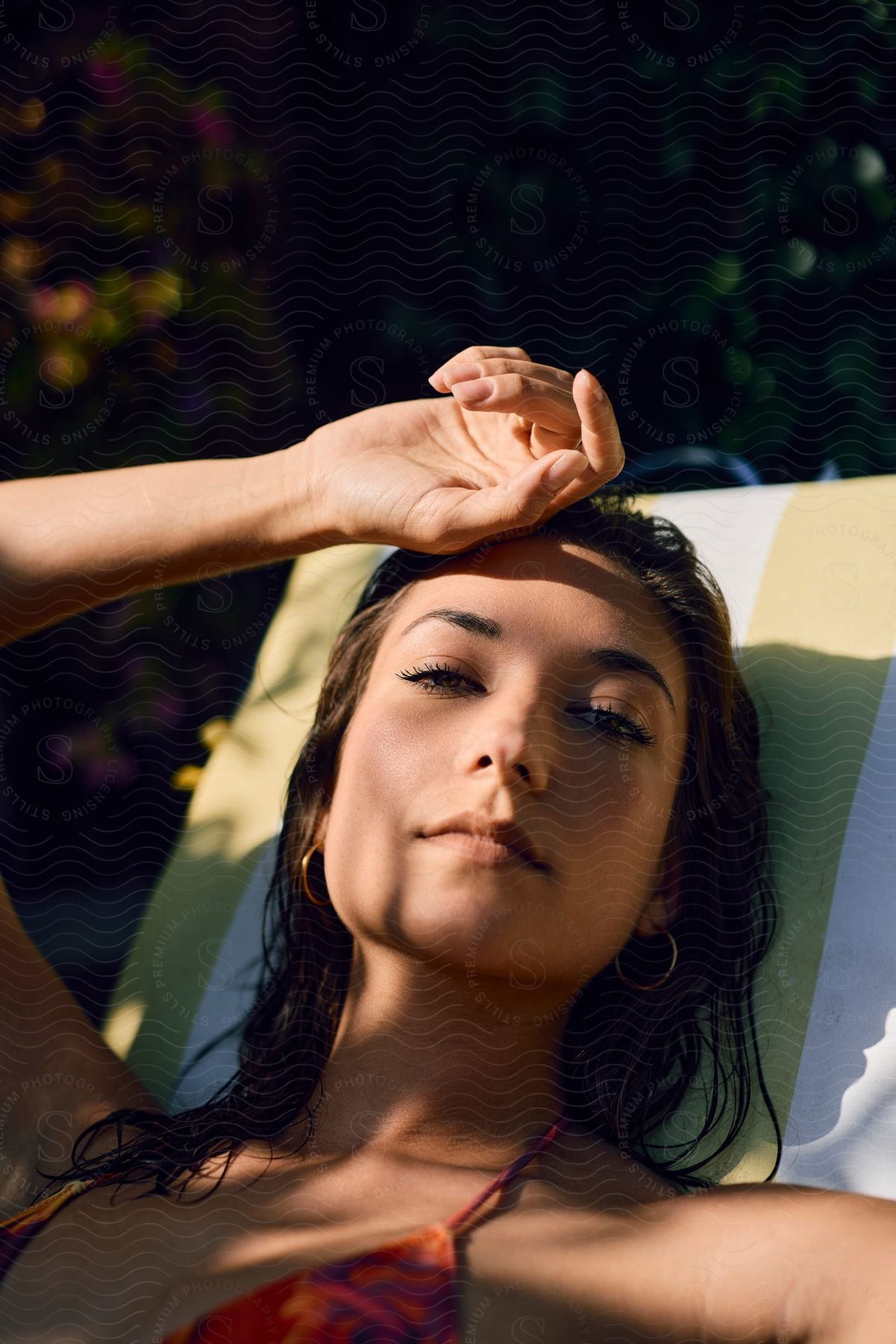 Portrait of a woman with wet hair lying on a sun lounger outdoors with her hand over her forehead.