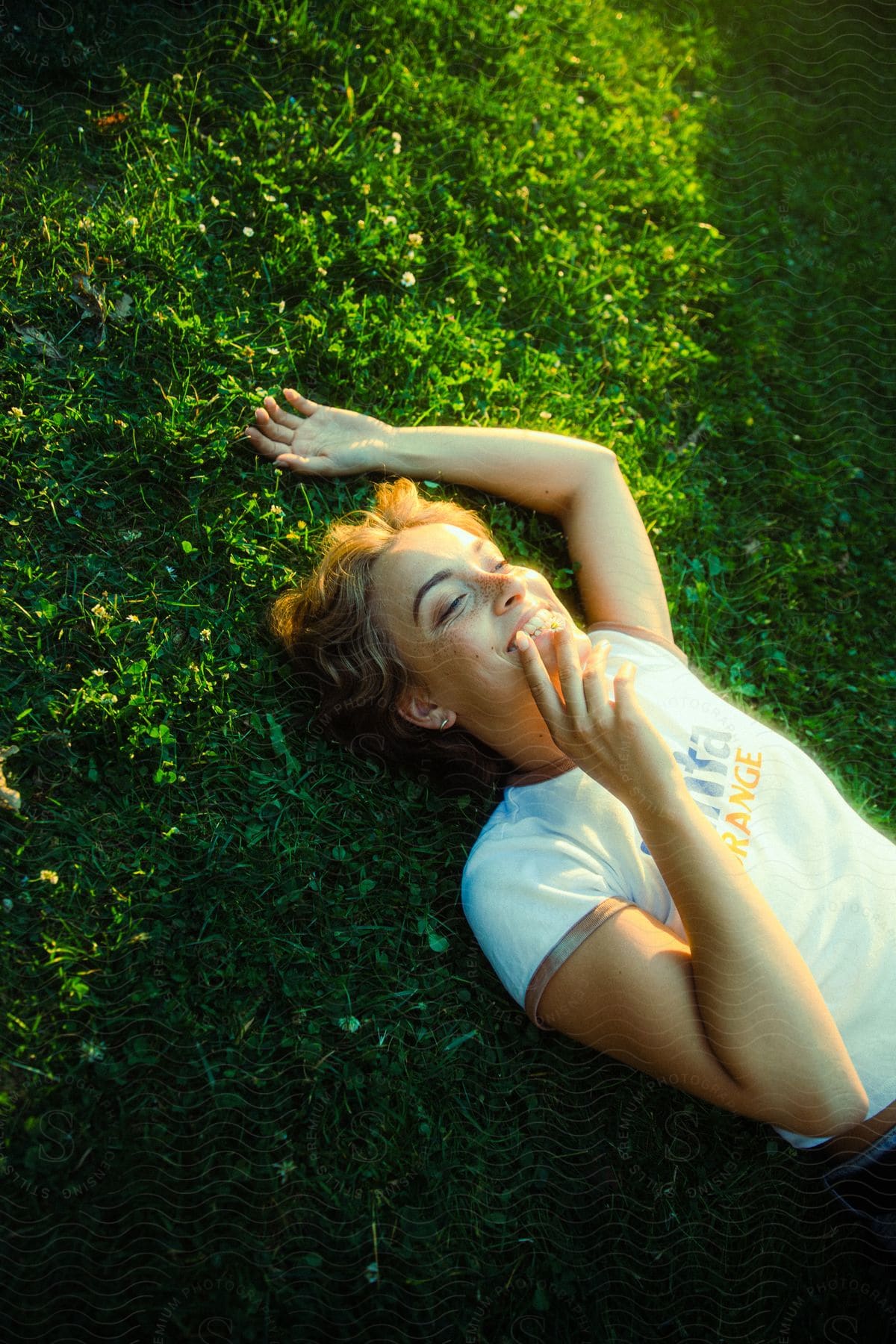 A woman is lying on a grassy field, smiling, and facing the sky during the daytime.