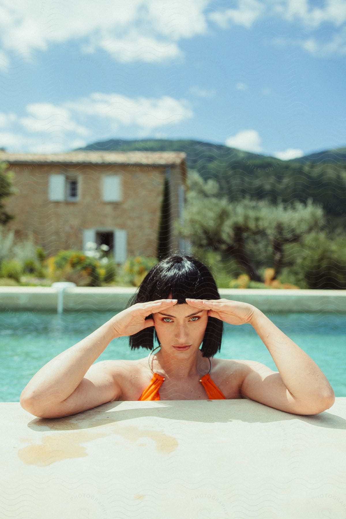 a stylish woman with a bob hairstyle wearing a vibrant orange bikini, standing beside a sparkling pool.