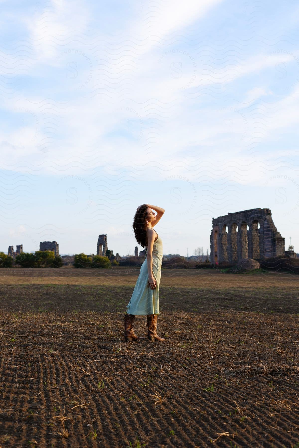 A woman models clothing in a field, with the ruins of Aqua Claudia in the background.