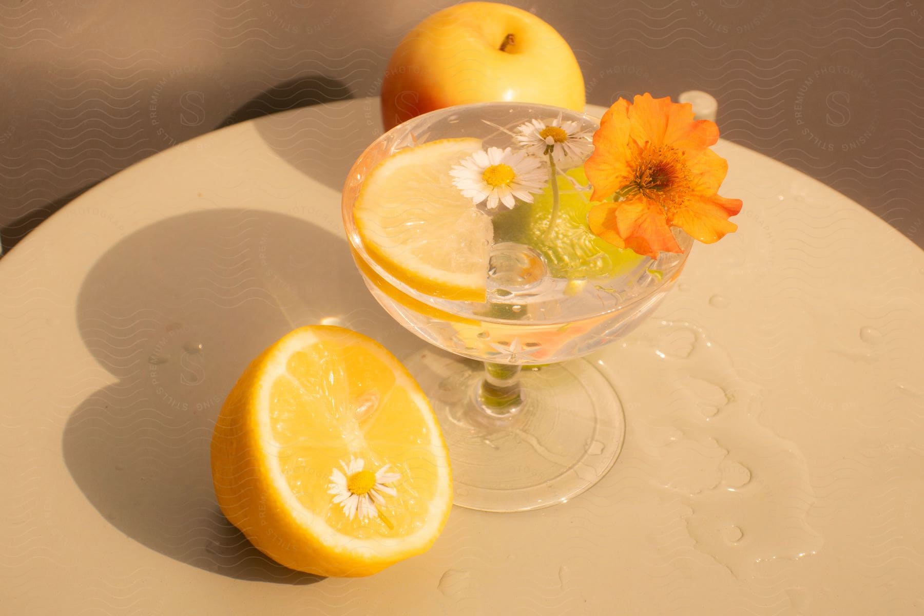 Drink with flowers or a slice of orange on the side and an apple in the background