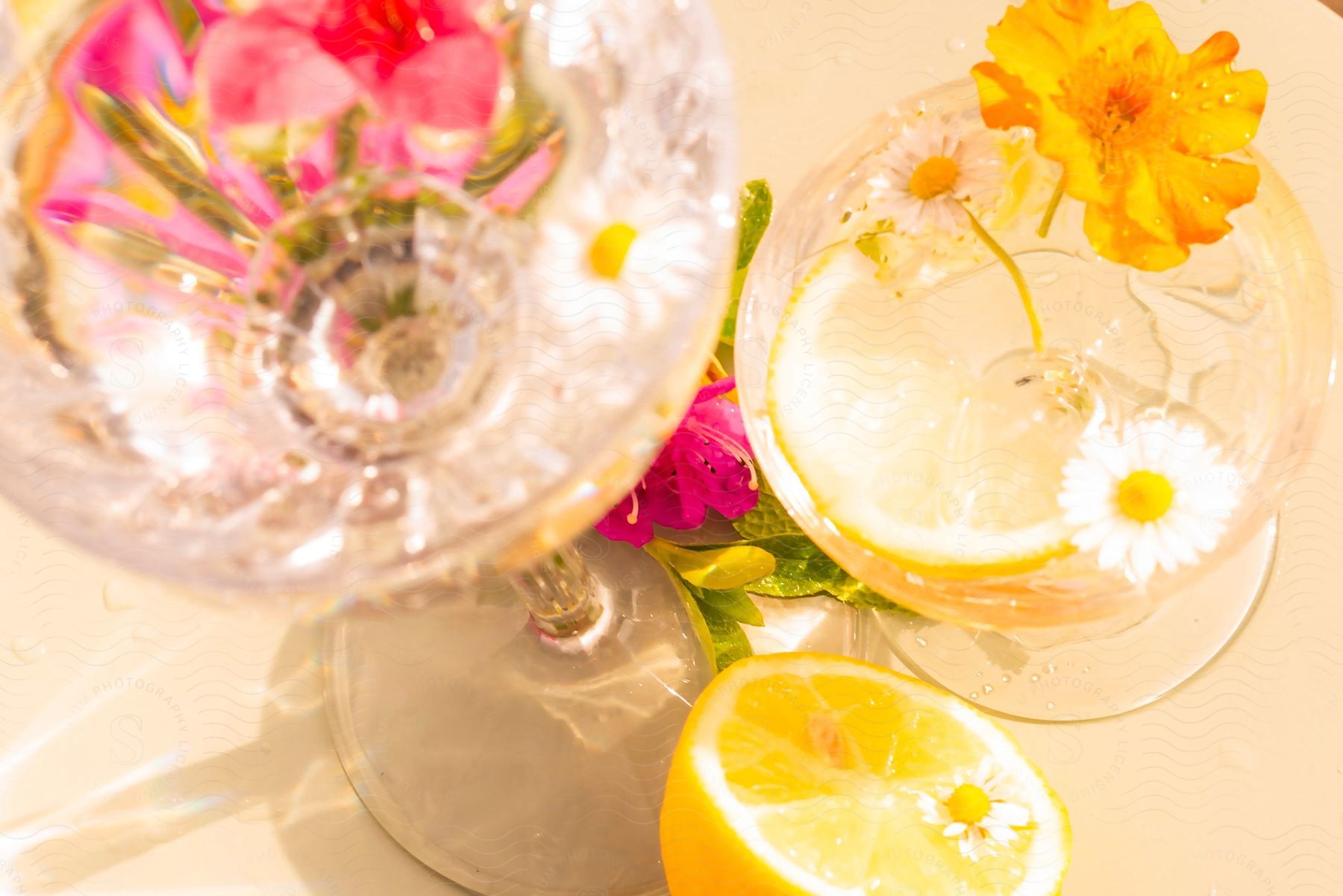 Glass glasses with flowers and a slice of lemon and another half of lemon next to the glass.