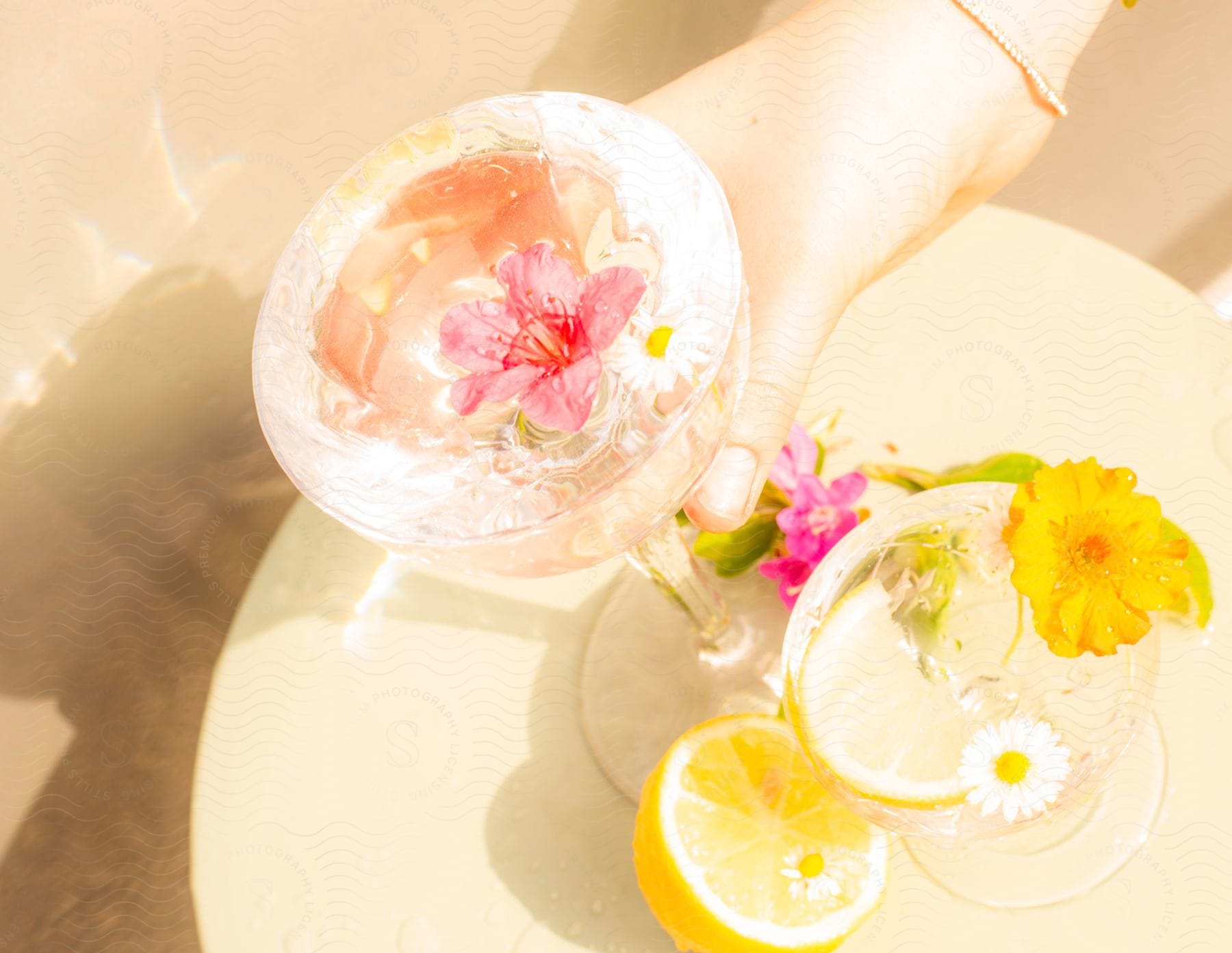 A person's hand is on a  fancy drink that is on table with another drink and lemon.