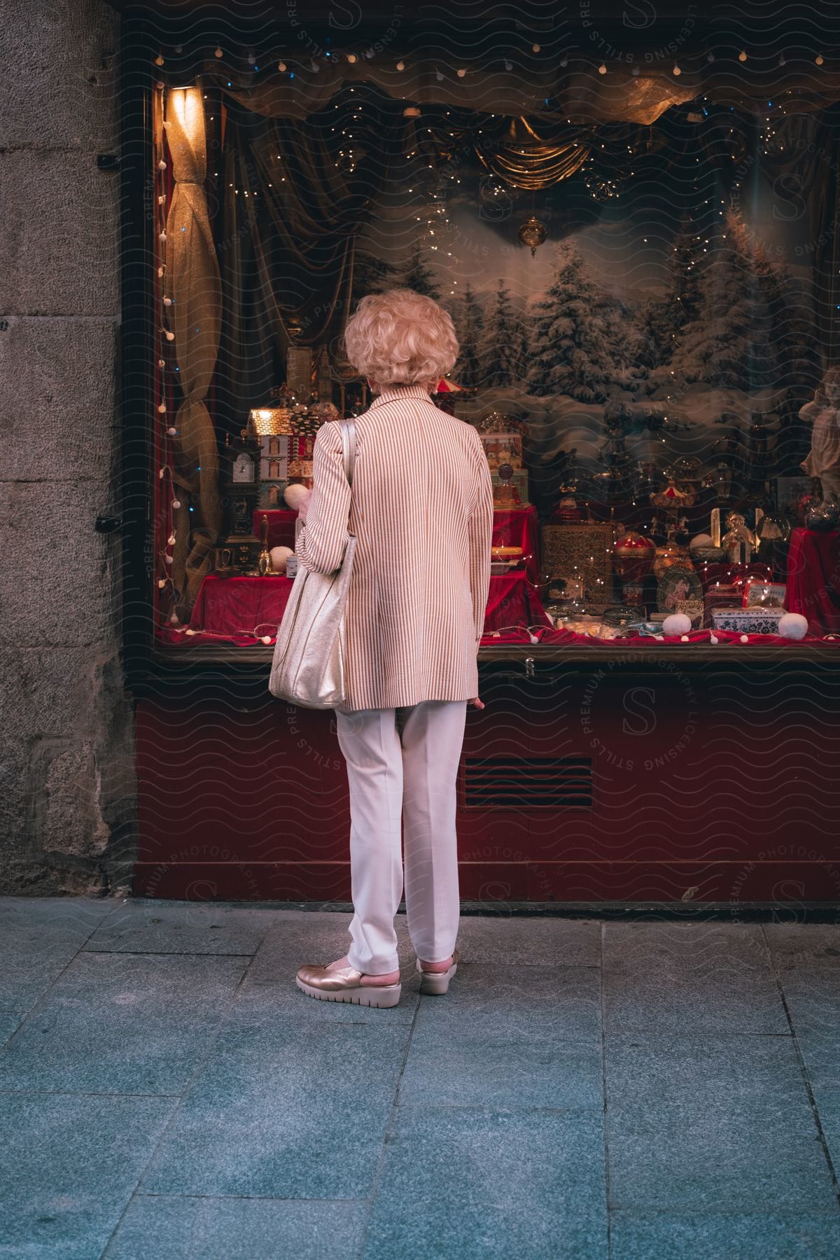 Someone looking at a festive shop window decorated for the holidays. The window displays a snowy backdrop, ornaments and items related to the holiday.