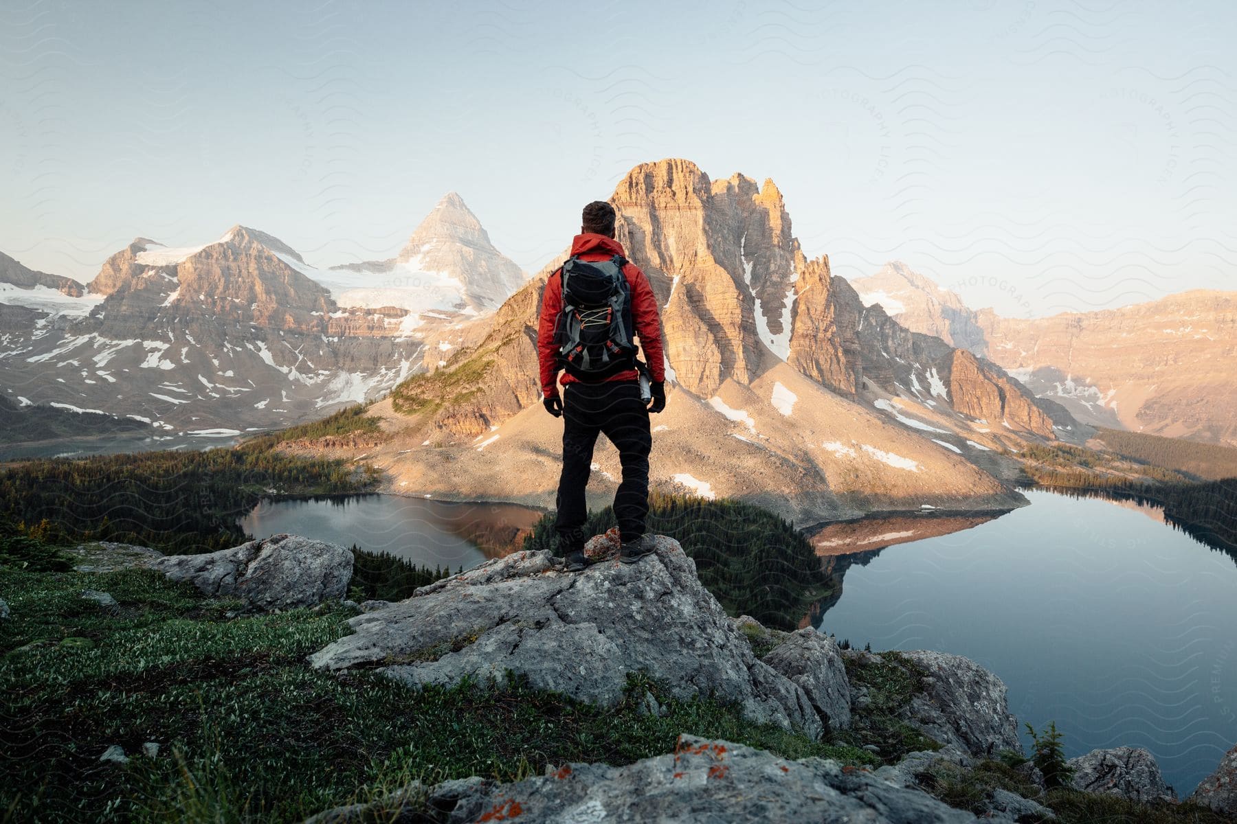 Hiker standing on a rocks overlooking a lake and mountains as he looks ahead