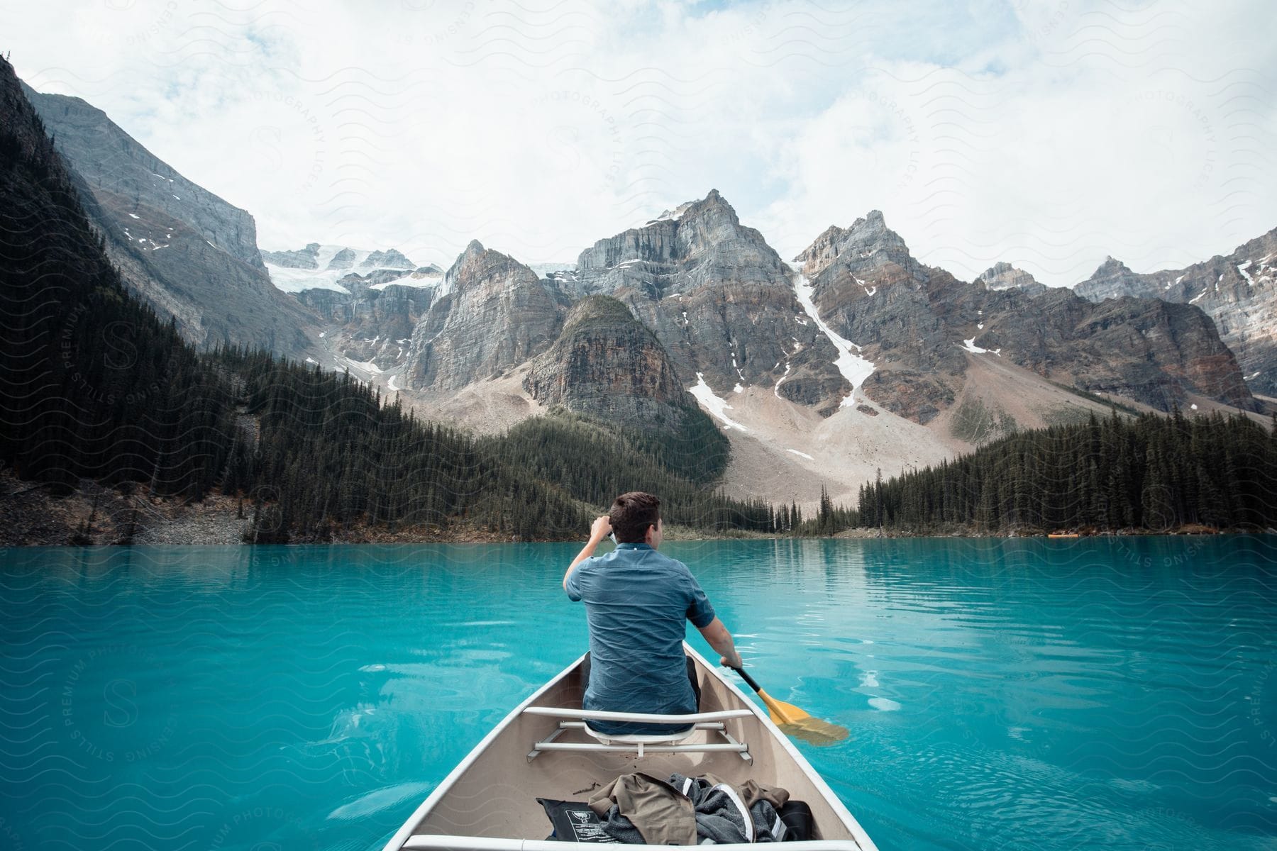 Man in a canoe paddling on a turquoise lake surrounded by forest and mountains