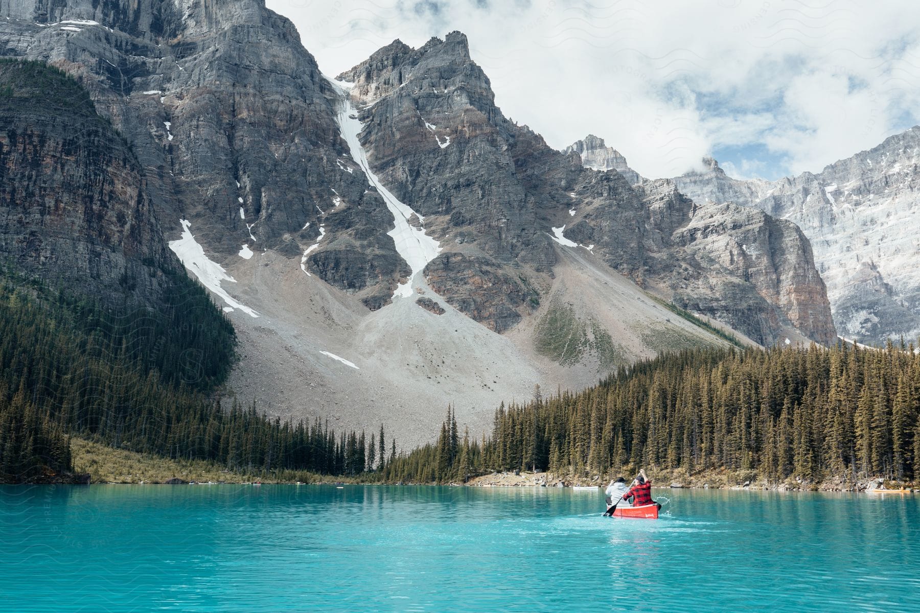 Man rows a canoe on clear blue water with forests and mountains along the coast