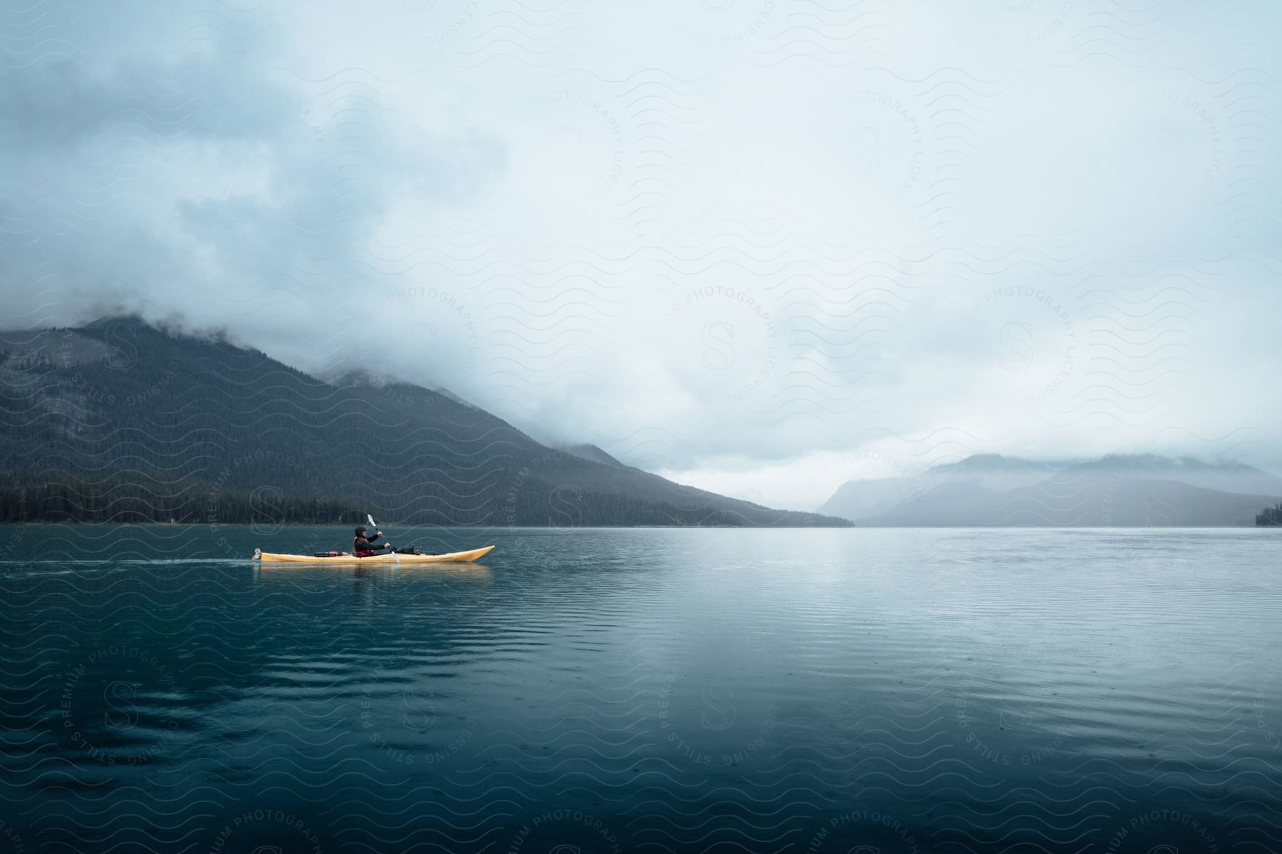 Man rows a canoe across the water with mountains along the coast