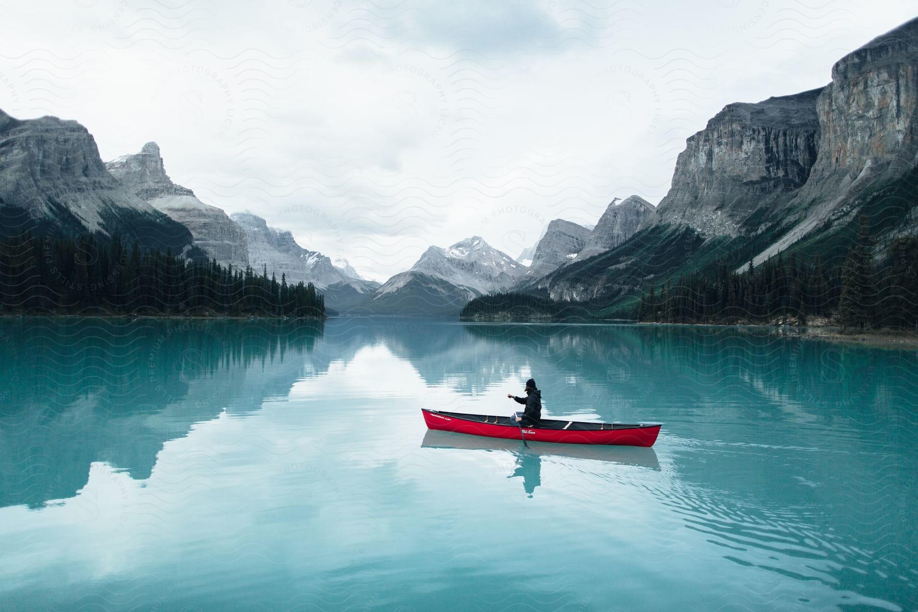 A man paddling a red canoe on a serene lake