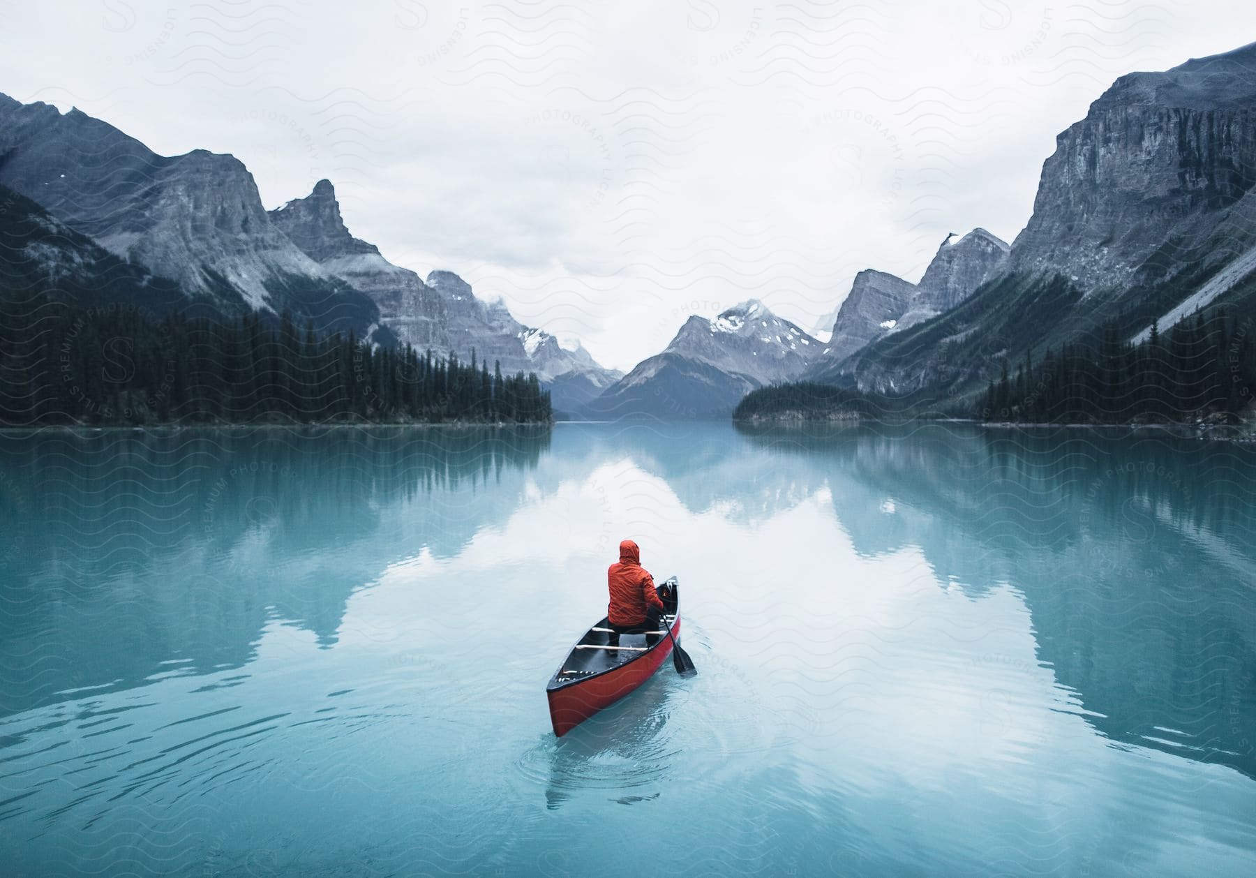 Man rows a canoe on a river between forested mountains on a winter day