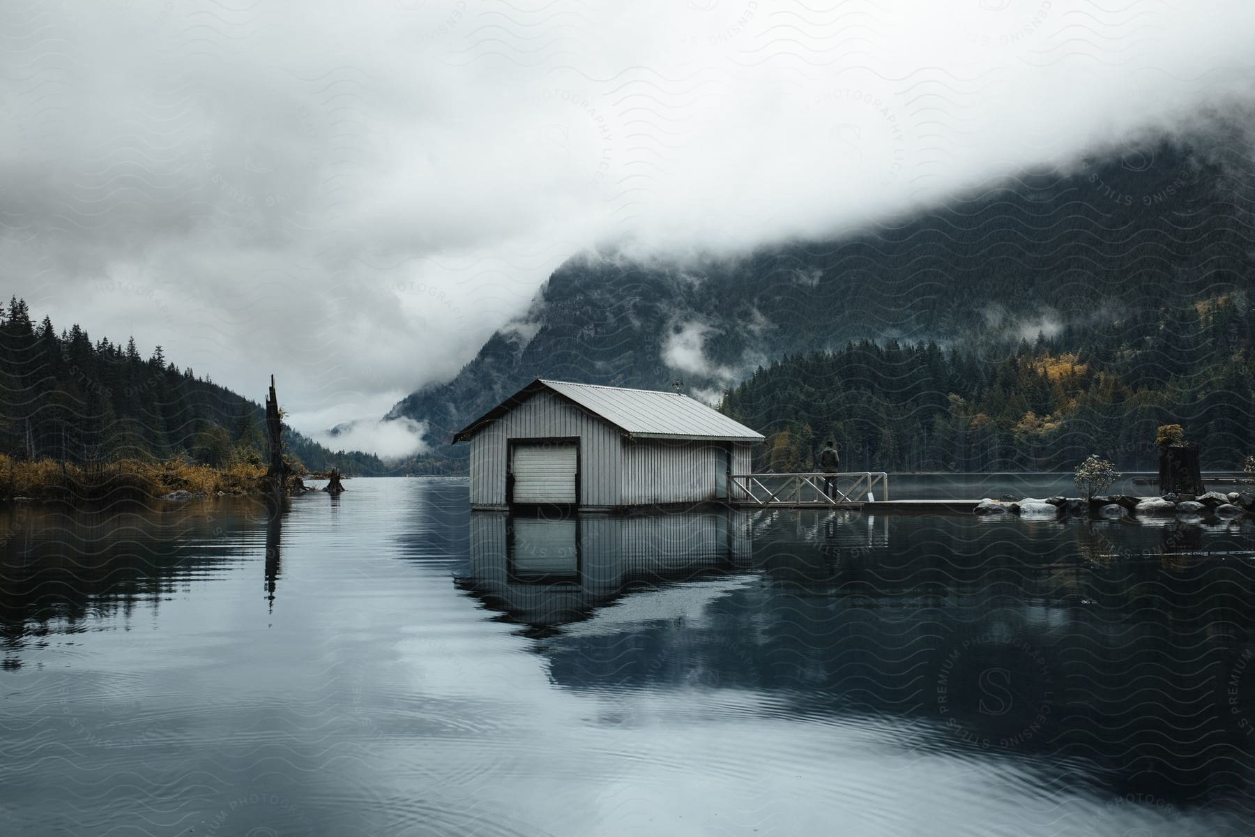 A house on stilts surrounded by a calm lake and misty mountains.