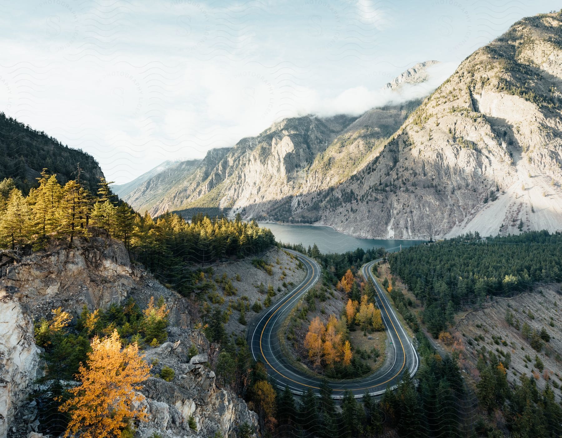 Scenery of a winding asphalt road by a lake with mountains around