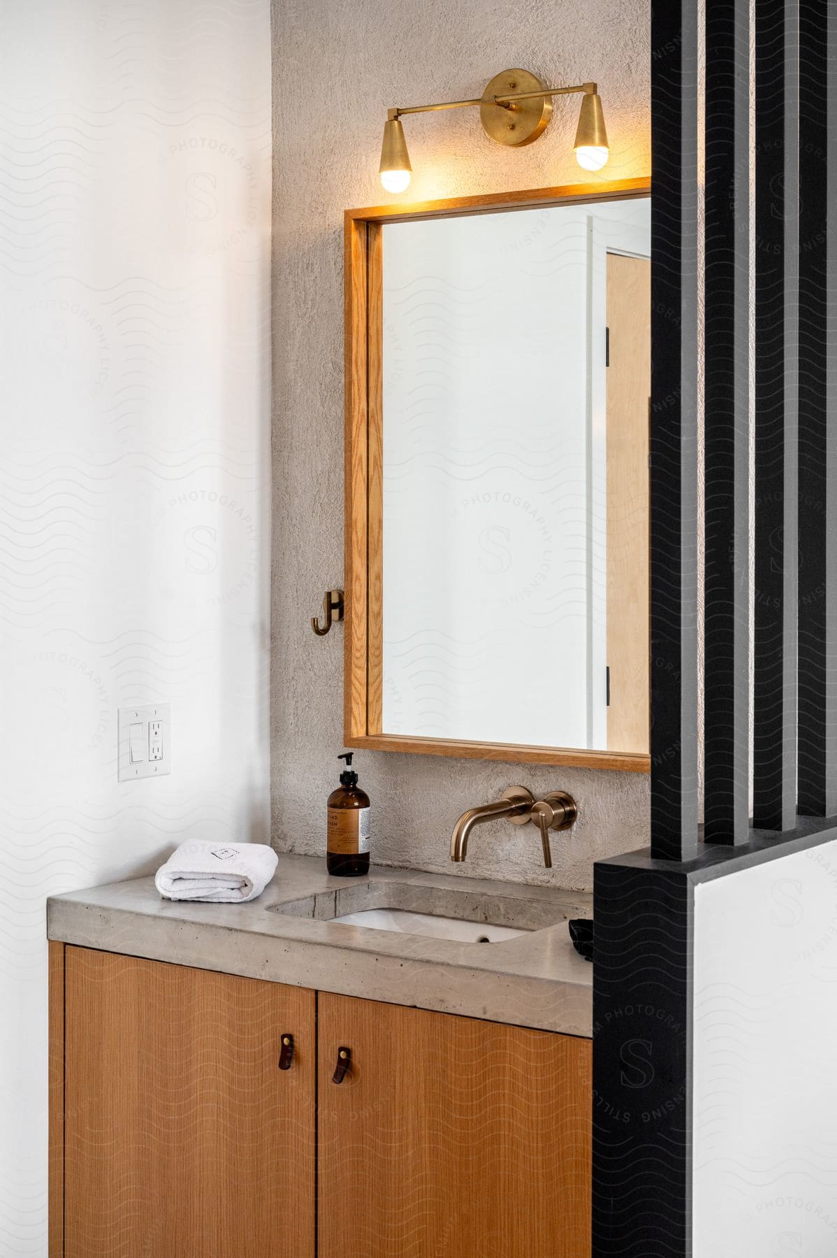 A modern bathroom sink area with a large mirror, illuminated by wall lights. The concrete worktop and wooden cabinet complete the look.