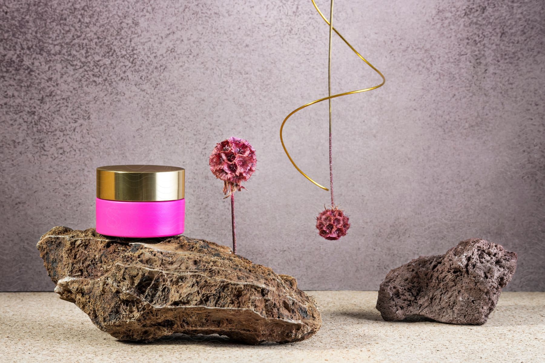 A pink container with a lid sits on a smooth, gray rock.