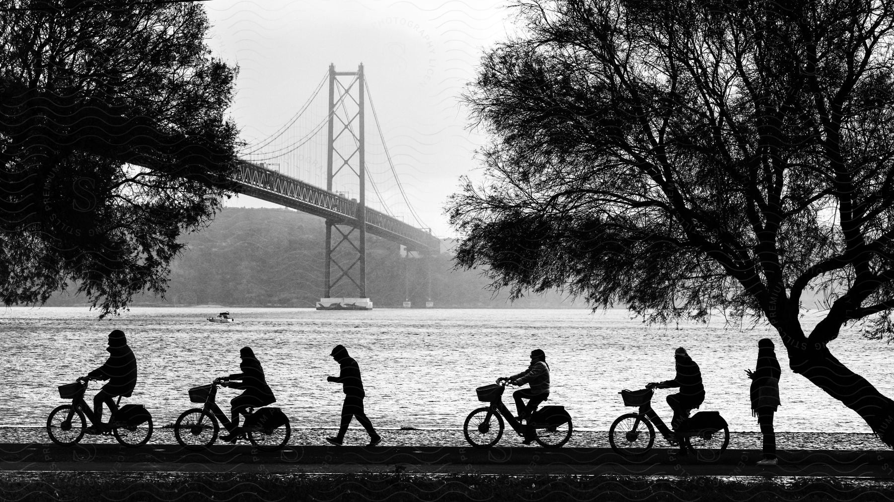 A group of people walks and cycle by the sea with a suspension bridge in the background