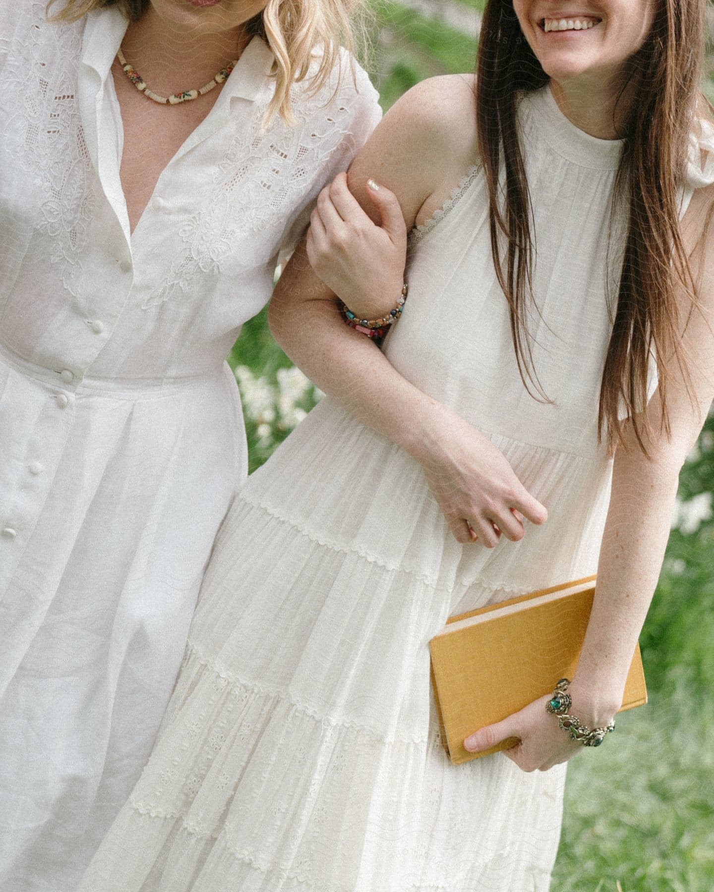 two friends arm in arm are walking together outdoors and holding a book