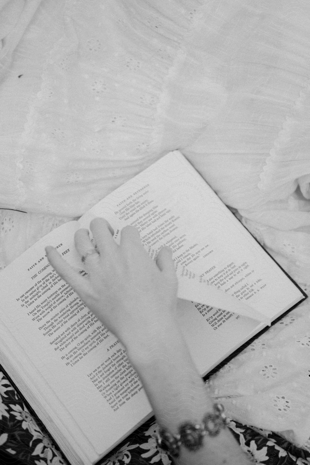 a woman wearing a ring, a bracelet, and a white dress as she turns the page of a book.